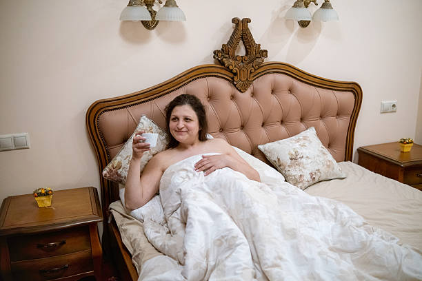 A woman relaxes in bed while sipping from a mug, showcasing a cozy morning scene filled with tranquility and comfort in a beautifully decorated bedroom.