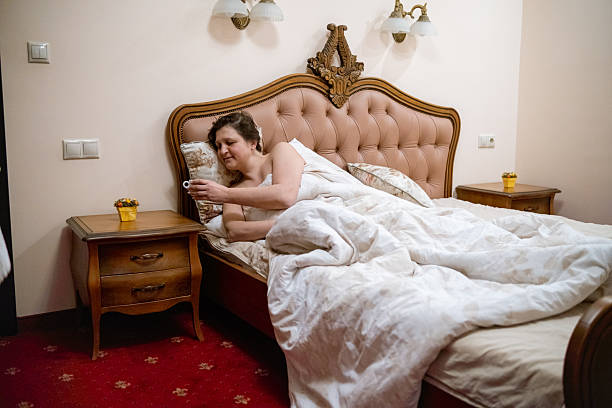 A woman relaxes in bed while sipping from a mug, showcasing a cozy morning scene filled with tranquility and comfort in a beautifully decorated bedroom.