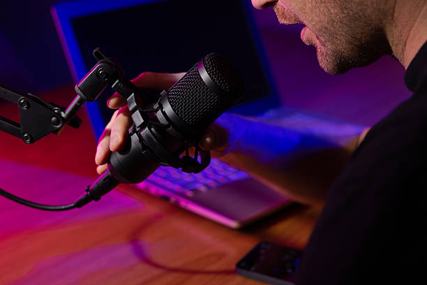 istock man talking in microphone in broadcasting studio with neon lights. podcast recording, streaming 2249778475