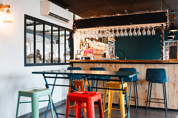 istock Empty modern french microbrewery interior featuring colorful metal stools, a wooden bar counter with taps, and a view of brewing tanks 2249785803