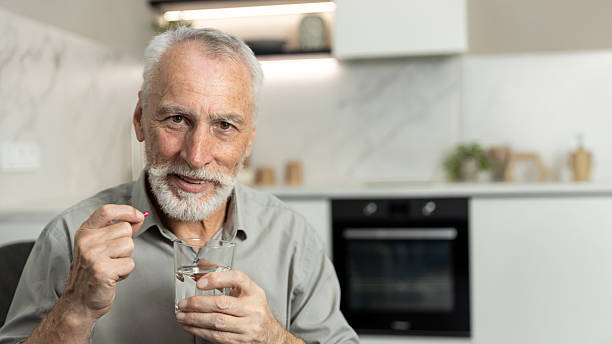 istock Senior man takes pill with water in a modern kitchen setting during the day 2249786240