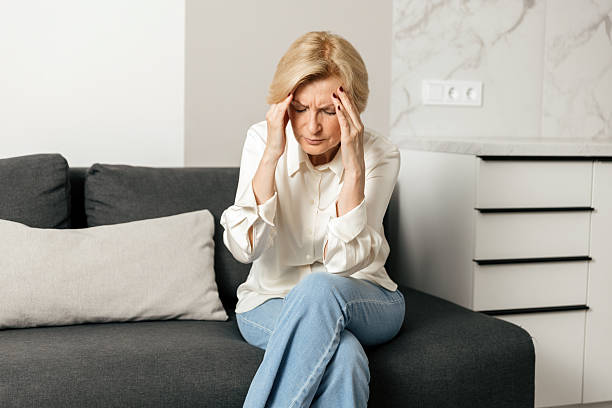istock Middle-aged woman holding her head on a couch while dealing with headache discomfort 2249786324