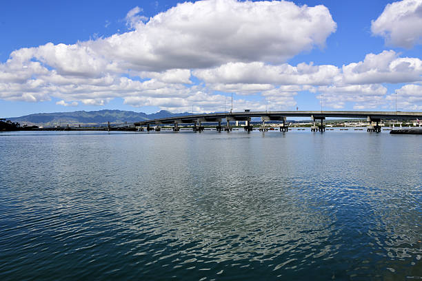 Honolulu, Hawaii, USA: Admiral Clarey Bridge, commonly known as the Ford Island Bridge, connecting the mainland of Oahu to Ford Island within Joint Base Pearl Harbor-Hickam. Opened in 1998, this 4,672-foot structure features a unique floating concrete pontoon design with a movable 930-foot drawspan, the largest of its kind in the world, to allow naval vessels to pass. The low-profile bridge, named after Admiral Bernard A. Clarey, replaced earlier ferry services, providing vital access to the historic naval sites and military housing on the island. Floating section on the left.