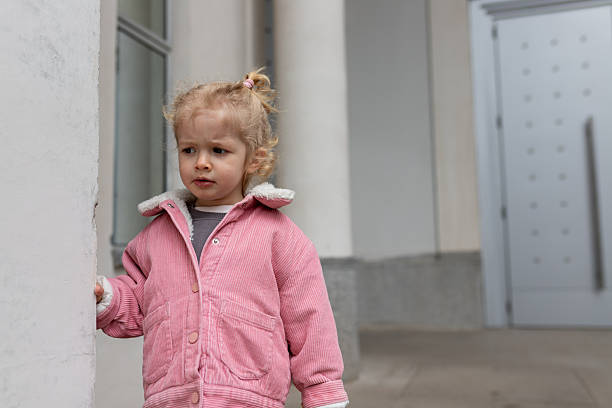 Curly blond toddler girl in the corner of the playground feeling sad and rejected by other kids