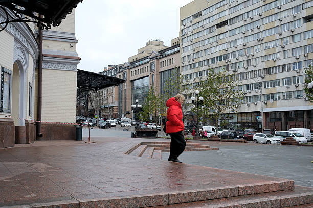 A person in a red jacket walks alone in a quiet urban square during rain. Kyiv, Ukraine, November 26, 2025.
