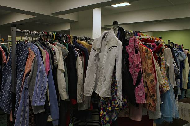 Long rows of clothing racks filled with various second-hand garments, including shirts, jackets, and colorful patterned dresses inside a thrift store or warehouse