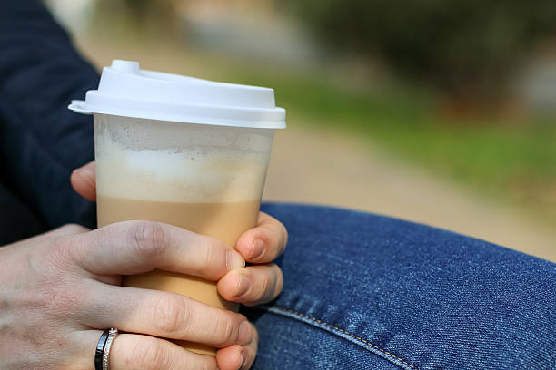 istock Seated person holding coffee cup beside mobile phone on bench 2249804626
