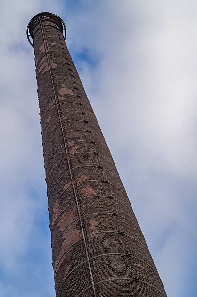 Tall, weathered brick chimney rising against a backdrop of clouds, showcasing industrial architecture