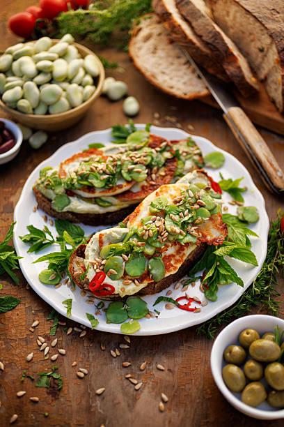 Sandwiches with broad bean spread and grilled goat cheese sprinkled with roasted sunflower seeds and fresh mint on a ceramic plate, close-up
