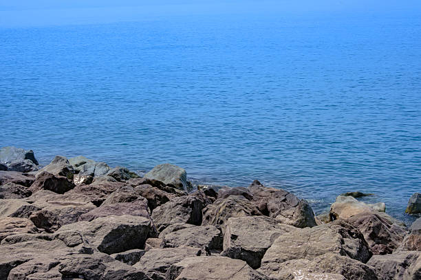 Large rocks form a natural barrier against the expansive, deep blue sea water under a clear summer sky. Creating a peaceful marine landscape view. Excellent background for designs.