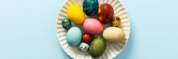 istock Beautifully decorated Easter eggs in vibrant colors are displayed on a white plate against a light blue background, symbolizing the joy of Easter festivities, banner 2249819473