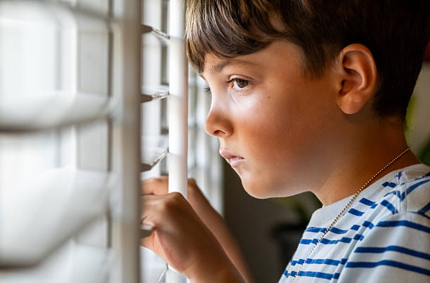 istock Serious sad little boy looking through a window 2249821039