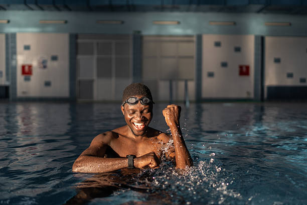 Swimmer in a swimming pool celebrating success, raising his fist, feeling happy and excited after a victorious swim while wearing goggles and a smartwatch