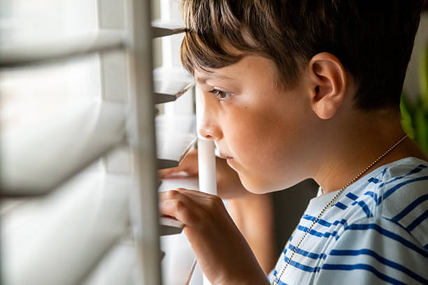 istock Serious sad little boy looking through a window 2249821516