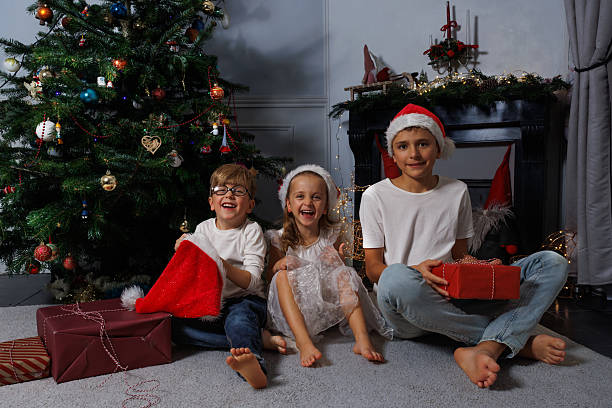 istock Smiling children playfully sitting together by a Christmas tree 2249822291