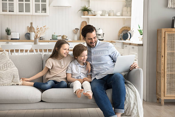 istock Smiling dad hugging kids on sofa showing video on notebook 2249824977