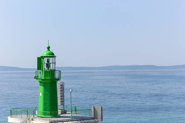 A vibrant green lighthouse stands prominently against the serene blue seascape. The calm scenery emphasizes simplicity and tranquility, ideal for concepts of guidance, direction, and coastal landscapes.