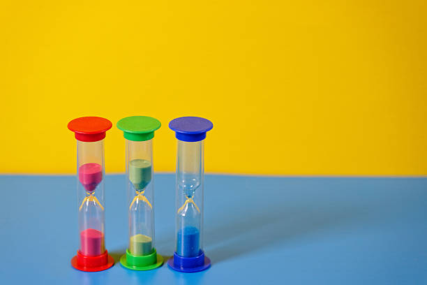 Transparent Glass Hourglasses with colorful sand on blue and yellow background as symbol of time. Selective focus