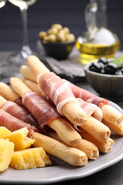 Grissini breadsticks with prosciutto and cheese on grey table, closeup