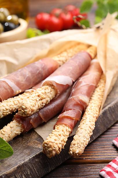 Grissini breadsticks with prosciutto on wooden table, closeup