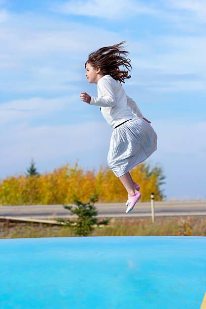 woman jumping on trampoline in jeans and white shirt near lush green forest