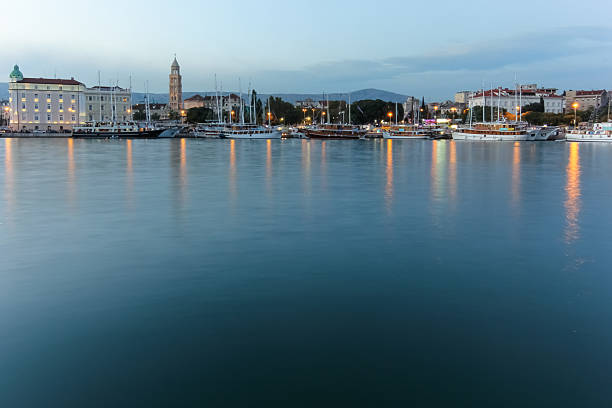A picturesque view of Split's waterfront featuring historical landmarks, palm-lined promenade, and scenic mountain backdrop under a clear blue sky.
