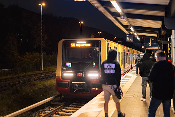 Berlin, Germany – October 16, 2025: An S46 S-Bahn train to Königs Wusterhausen arrives at a Berlin station platform at night as passengers wait along the edge of the platform. Deutsche bahn company.