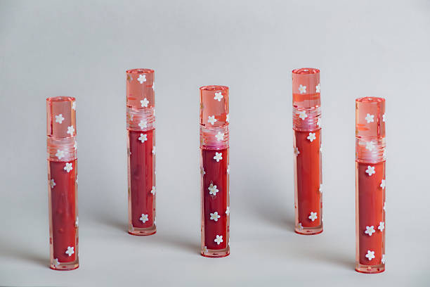 istock Five small red lipstick bottles with white floral motifs sit in a row on a pristine white surface;delicate branding and compact design create a charming feminine flatlay perfect for beauty stock. 2249864255