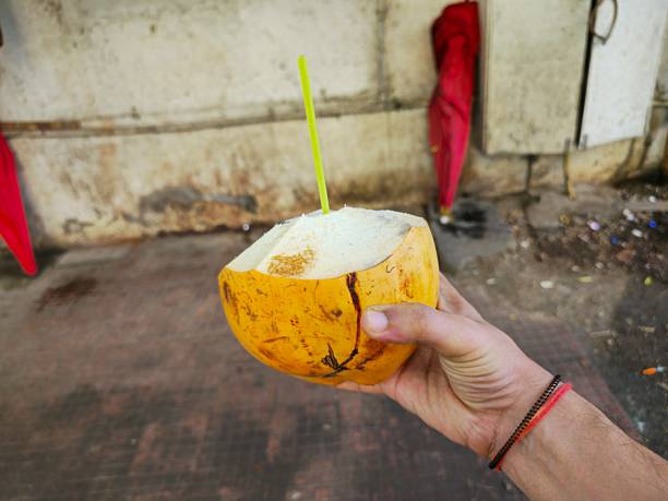 istock Fresh Tender Coconut with Straw Held in Hand on Street Side Background 2249864480