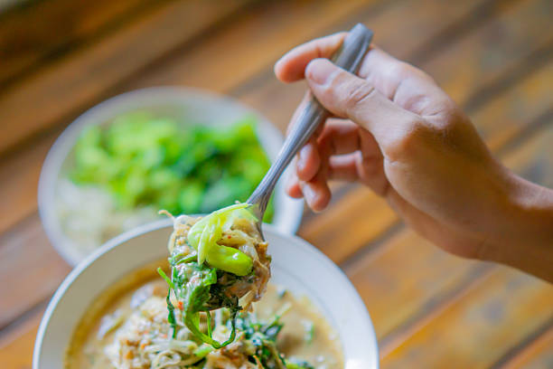 istock Hand scooping pecel. Pecel is a traditional Javanese salad consisting of boiled vegetables such as spinach, long beans, and bean sprouts drizzled with peanut sauce. 2249871581