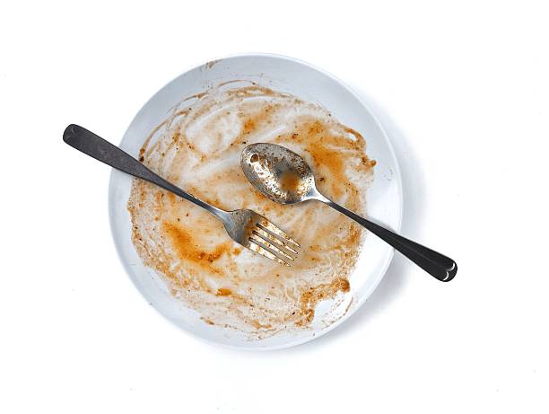 istock Dirty white plate with leftovers food with spoon and fork on top isolated on white background 2249883131
