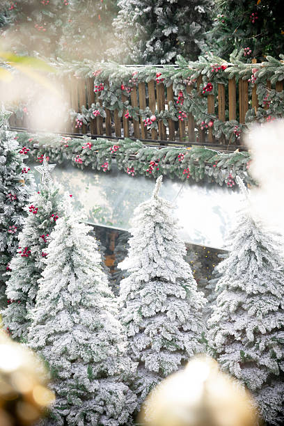 istock A festive winter scene featuring snow-covered Christmas trees adorned with red berries and garlands, set against a wooden fence decorated for the holidays 2249884753