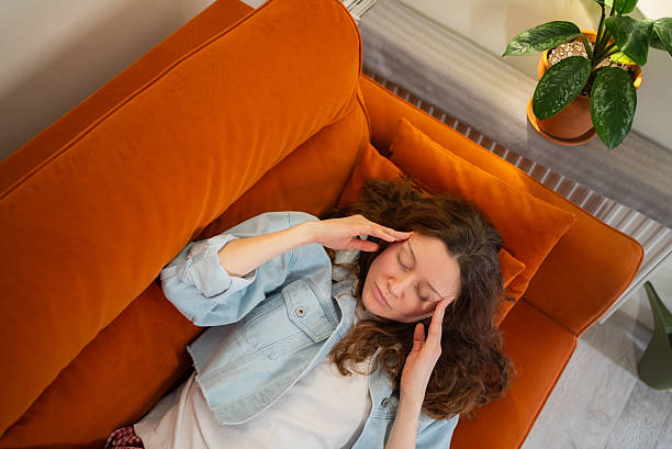istock Woman experiencing intense headache lying on orange sofa, eyes closed, hands pressing temples, suffering from painful migraine and stress 2249884916