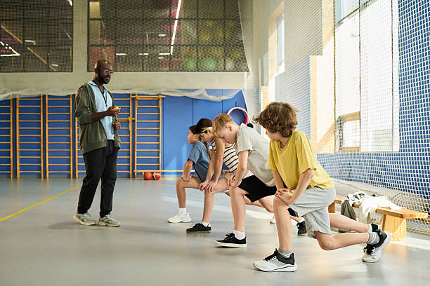 istock Black Man Coaching Group of Children Stretching Legs during Physical Education 2249891593