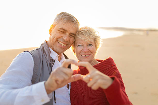 istock Happy senior couple making heart shape with hands on beach at sunset 2249892482