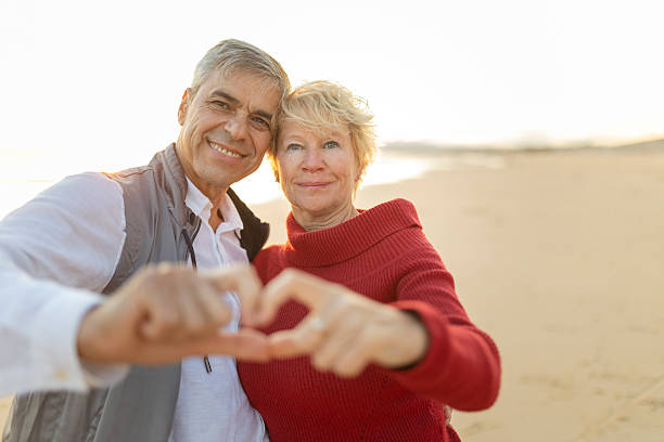 istock Happy senior couple making heart shape with hands on beach at sunset 2249892775