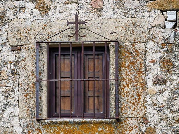 Trujillo, Cáceres, Spain, November 30, 2025: Medieval window with a wrought iron cross on a rustic stone wall