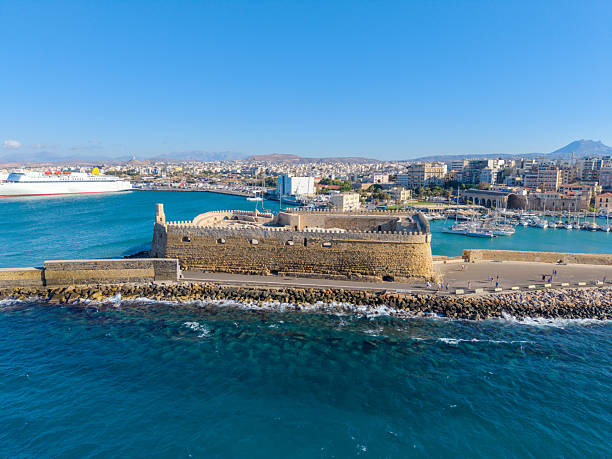 Heraklion Port in Crete, Greece, with ferries, blue waters, and the historic Venetian Koules Fortress overlooking the harbor.\