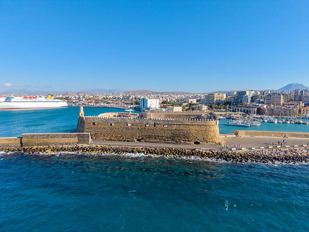 Heraklion Port in Crete, Greece, with ferries, blue waters, and the historic Venetian Koules Fortress overlooking the harbor.\