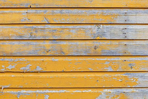 Close-up of texture of weathered wooden siding with peeling yellow paint, Orimattila, Finland.