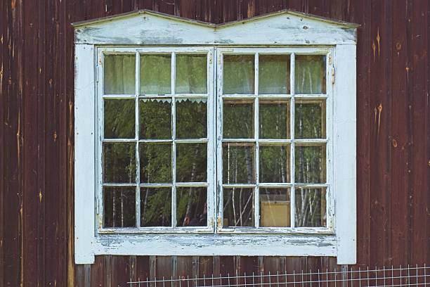 Old traditional Scandinavian wooden house window, set against a dark red wood wall, Päijänne, Finland.