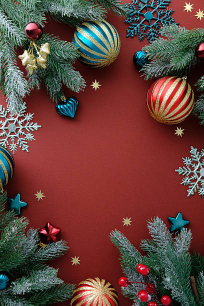 istock Vertical Christmas background with vintage ornaments, pine branches, snowflakes, confetti on dark red table. Happy New Year poster template. Xmas frame 2249897738