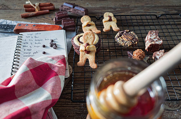 A warm and inviting kitchen scene captures sugar cookies cooling beside a recipe notebook, with a honey jar and dipper gently blurred in the foreground. Cinnamon sticks and rich chocolate pieces add layers of texture and flavor. A red napkin enhances the festive mood, emphasizing the sustainable joy of homemade holiday baking.