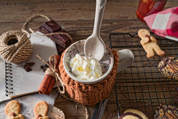 An inviting mug of hot chocolate wrapped in a handmade knitted sleeve sits at the center of a rustic holiday baking flat lay. Surrounded by chocolate bars, cinnamon sticks tied with jute, and a handwritten cookie recipe, the scene captures the spirit of slow, sustainable Christmas traditions. There’s room for text in the upper left and right corners.