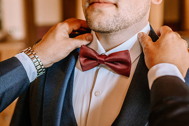 istock Man in formal attire adjusts his red bow tie with assistance, showcasing a moment of preparation for a special event, emphasizing elegance and attention to detail 2249897943