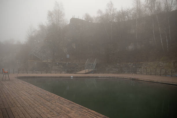 Foggy outdoor swimming pool surrounded by trees and wooden deck. Zakrzowek, Krakow