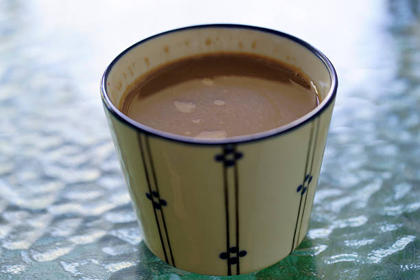 A beautifully designed ceramic cup filled with warm coffee rests on a textured glass table. The scene captures a cozy and inviting moment, perfect for coffee lovers.