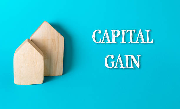 Wooden house-shaped blocks representing capital gain on a vibrant turquoise background, illustrating financial growth and investment concepts in a modern business context