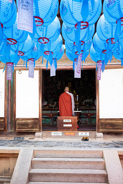 Gyeongju, South Korea November 13, 2025. Buddhist monk reverently standing inside a temple, surrounded by decorative blue paper lanterns, engaging in deep prayer and devotion