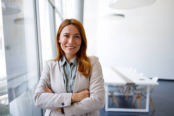 istock Professional woman standing at an office window, smiling looking at the camera, showing confidence and success 2249910708
